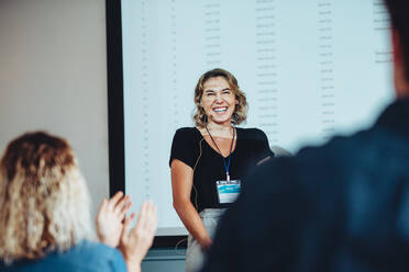 Eine Geschäftsfrau lächelt mit dem Publikum, das bei einer Konferenz in die Hände klatscht. Weibliche Fachleute erhalten Applaus von den Teilnehmern einer Konferenz. - JLPSF15454