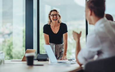 Businesswoman standing at conference table and laughing. Female professional smiling during a meeting in office boardroom. - JLPSF15459