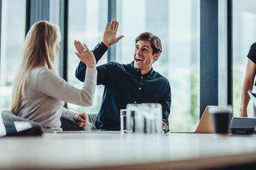 Glückliche und erfolgreiche Geschäftskollegen geben sich im Büro die Hand. Mitarbeiter sitzen im Konferenzraum und feiern ihren Erfolg. - JLPSF15462