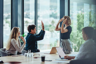 Zwei Kollegen geben sich in einer Besprechung ein High Five. Geschäftsleute feiern ihren Erfolg im Konferenzraum. - JLPSF15467