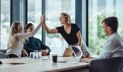 Eine Frau gibt ihrem Kollegen im Konferenzraum ein High Five. Eine Gruppe von Kollegen feiert ihren Erfolg in einer Sitzung. - JLPSF15469