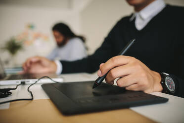 Businessman writing on a digital writing pad to input data into a computer. Close up of a man holding a digital pen writing on a digital writing pad in office. - JLPSF15482