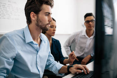 Softwareentwickler sitzen vor einem Computer und arbeiten im Büro. Zwei Männer und eine Frau schauen auf einen Computer und entwickeln Anwendungen im Büro. - JLPSF15504