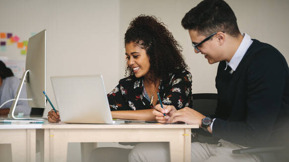 Geschäftsmann und Frau besprechen die Arbeit und schreiben Notizen im Büro sitzend. Geschäftspartner arbeiten zusammen sitzend am Schreibtisch mit Laptop-Computer. - JLPSF15510