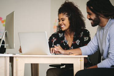 Geschäftspartner tauschen Ideen aus, die am Schreibtisch mit einem Laptop sitzen. Glückliche Geschäftskollegen im Büro, die gemeinsam an einem Projekt arbeiten. - JLPSF15531