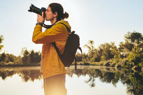 Seitenansicht eines Touristen, der mit einer DSLR-Kamera ein Foto macht. Ein Mann, der die Schönheit der Natur in der Nähe eines Sees festhält. - JLPSF15572