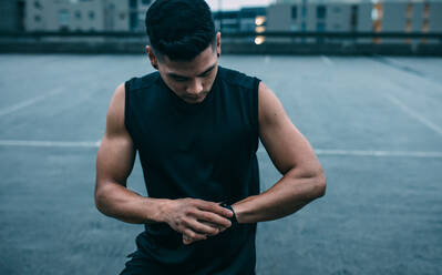 Muskulöser Mann, der seine Leistung mit der Fitness-App auf seiner Smartwatch überprüft. Männlicher Sportler, der eine Smartwatch benutzt, um seine Fortschritte zu überwachen. - JLPSF15585