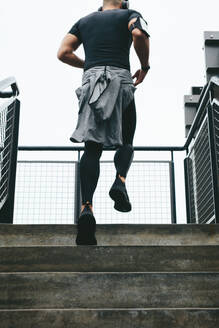 Rückansicht eines jungen Mannes, der die Treppe hinaufläuft. Ein fitter Mann in Sportkleidung trainiert auf der Treppe. - JLPSF15594