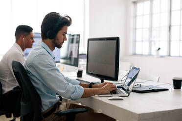 Softwareentwickler sitzen im Büro und arbeiten mit Kopfhörern an Computern. Anwendungsentwickler arbeiten an einem Laptop im Büro. - JLPSF15606
