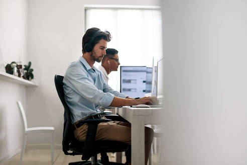 Softwareentwickler sitzen im Büro und arbeiten mit Kopfhörern an Computern. Anwendungsentwickler arbeiten an einem Laptop im Büro. - JLPSF15607