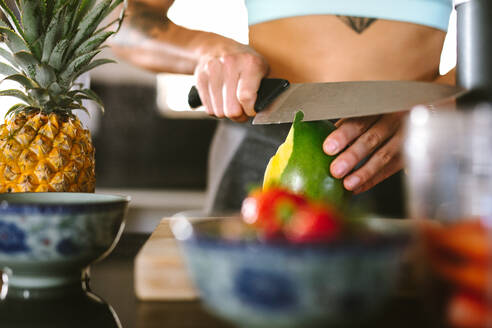 Nahaufnahme einer weiblichen Hand, die eine Frucht mit einem Messer am Küchentisch schält. Eine Frau macht einen Smoothie in der Küche. - JLPSF15628