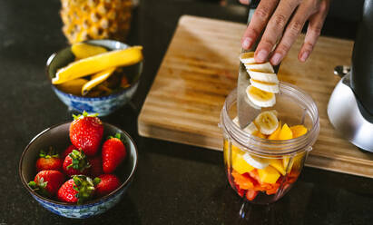 Hands of woman putting fruits in grinder bowl. Female making mix fruit smoothie in kitchen. - JLPSF15629