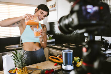 Frau gießt frischen Smoothie aus einer Saftpresse in ein Glas. Food-Bloggerin nimmt einen Vlog über frischen und gesunden Smoothie auf. - JLPSF15631