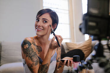 Beauty-Bloggerin, die ein Video-Tutorial mit der Kamera aufnimmt und zeigt, wie man Make-up aufträgt. Weibliche Vloggerin, die einen Make-up-Vlog für ihren Online-Kanal aufnimmt. - JLPSF15646