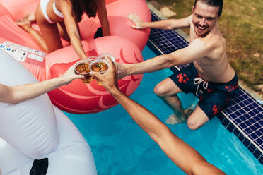 Eine Gruppe von Freunden, die in einem Pool feiern und Bier trinken. Freunde stoßen mit Bier auf einer Poolparty an. - JLPSF15676