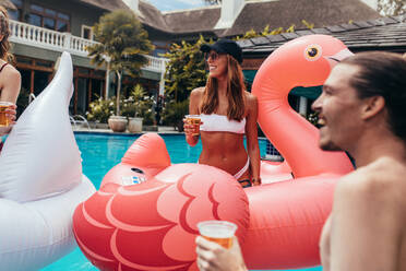 Frau im Bikini sitzt auf einem aufblasbaren Spielzeug und trinkt Bier mit Freunden bei einer Sommer-Poolparty. - JLPSF15677