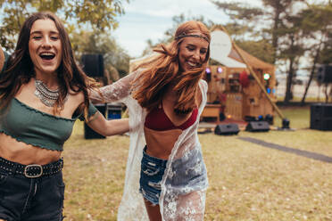 Two young women walking and dancing in the park. Hipsters enjoying a day at park during music festival. - JLPSF15689