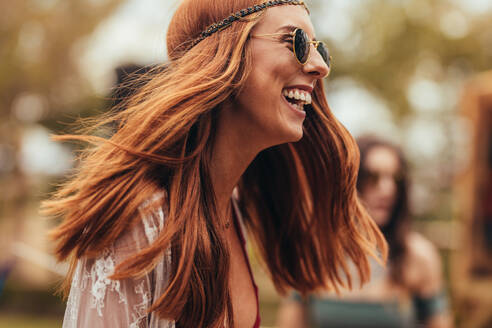 Lachende junge Frau im Retro-Look auf einem Musikfestival. Hübsche junge Frau mit Sonnenbrille im Park, lächelnd. - JLPSF15701