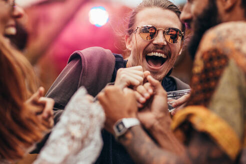 Fröhlicher Mann, der mit Freunden auf einem Musikfestival tanzt. Gruppe von Menschen, die sich auf einem Musikfestival amüsieren. - JLPSF15708