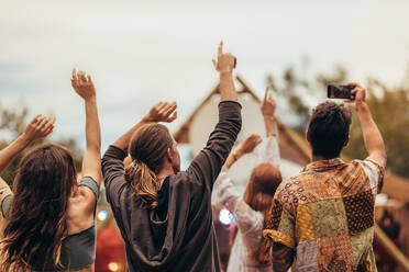 Rückansicht von jungen Leuten bei einem Musikkonzert. Gruppe von Männern und Frauen, die sich die Hände reichen und Fotos bei einem Musikfestival machen. - JLPSF15719