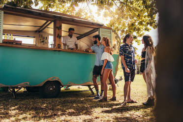 Young people buying street food from a food truck at park. Group of men and woman at food truck. - JLPSF15725