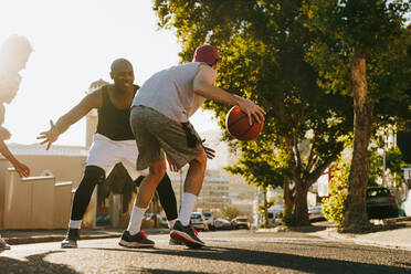 Männer beim Basketballspiel an einem sonnigen Tag auf einer leeren Straße. Vier Männer spielen Basketball auf der Straße. - JLPSF15727