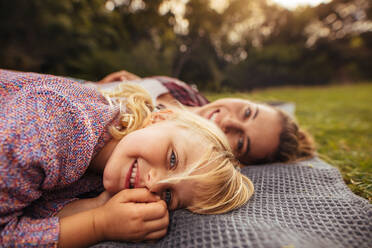 Little girl lying on plaid in front with her mother at the back at park. Young girl with her mother at a picnic in the park autumn - JLPSF15735