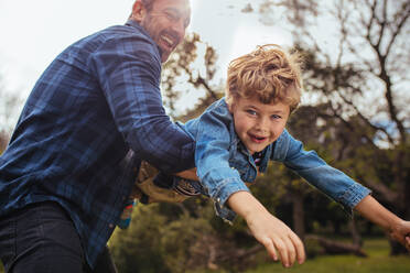 Little boy flying in arms of his dad. Small kid playing and having fun with his father at the park. - JLPSF15737