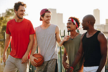 Vier fröhliche Basketballer, die auf dem Bürgersteig gehen und sich unterhalten. Männer, die nach einem Basketballspiel zurückgehen. - JLPSF15752