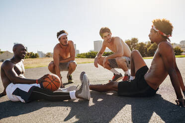 Basketballspieler sitzen auf dem Boden und unterhalten sich während einer Pause. Müde Männer entspannen sich nach einem Basketballspiel. - JLPSF15757