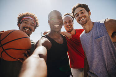 Vier Männer posieren für ein Selfie mit einem Basketball. Lächelnde Sportler, die sich beim Basketballspielen vergnügen. - JLPSF15761