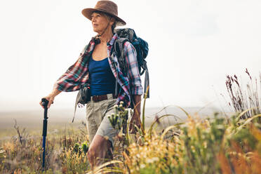 Ältere Frau auf einem Wanderausflug, die mit Hilfe eines Trekkingstocks läuft. Frau beim Trekking auf dem Lande, die durch die Büsche läuft. - JLPSF15782