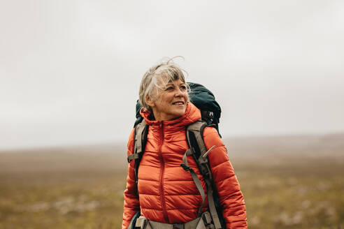 Ältere Frau steht mit Rucksack auf einem Hügel und schaut weg. Abenteuerlustige Frau beim Trekking auf einem Hügel. - JLPSF15797