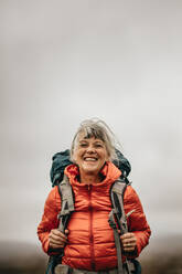 Senior woman hiker carrying a backpack trekking on a cloudy day. Happy woman on a vacation enjoying hiking. - JLPSF15807