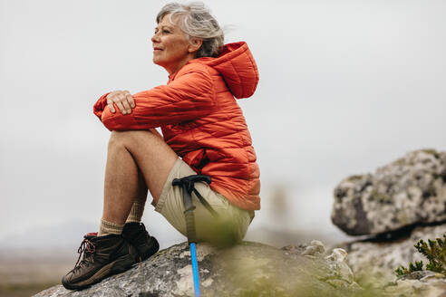 Nahaufnahme einer Frau, die auf einem Felsen sitzt und die Schönheit der Natur genießt. Ältere Frau entspannt sich nach ihrer Wanderung auf einem Hügel. - JLPSF15813