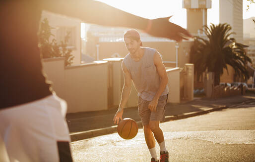 Junger Mann spielt mit Basketball auf der Straße. Mann übt Basketballspiel an einem sonnigen Tag auf einer leeren Straße. - JLPSF15818