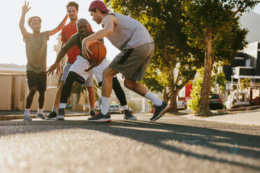 Männer spielen Basketball an einem sonnigen Tag auf einer leeren Straße. Männer üben Basketball-Dribbeln auf der Straße. - JLPSF15822