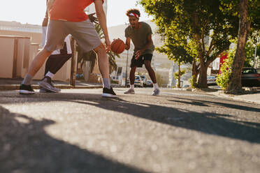 Männer spielen Basketball an einem sonnigen Tag auf einer leeren Straße. Männer üben Basketball-Dribbeln auf der Straße. - JLPSF15823