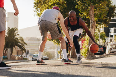 Männer spielen Basketball an einem sonnigen Tag auf einer leeren Straße. Männer üben Basketball-Dribbeln auf der Straße. - JLPSF15824