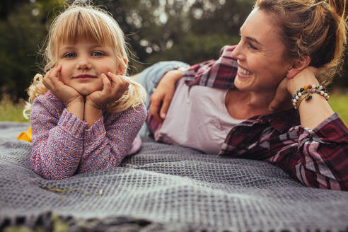 Kleines Mädchen und junge Frau liegen zusammen auf einer Decke im Park. Mutter und Tochter beim Picknick im Park. - JLPSF15828