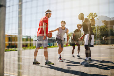 Vier Männer, die an einem sonnigen Tag auf einem Basketballplatz Basketball spielen und das Dribbeln üben. - JLPSF15854