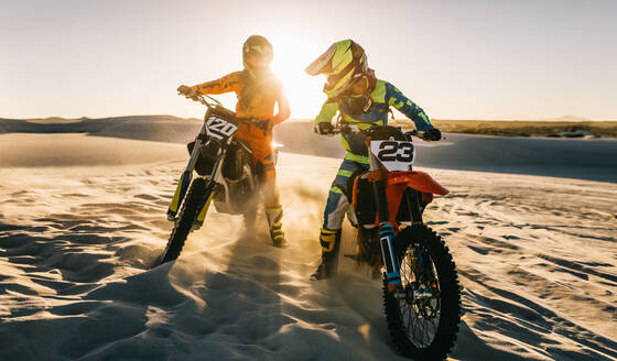 Zwei Motocross-Fahrer auf einer Wüstenpiste. Biker stehen auf einer Sanddüne und wirbeln den Sand beim Offroad-Training auf. - JLPSF15873