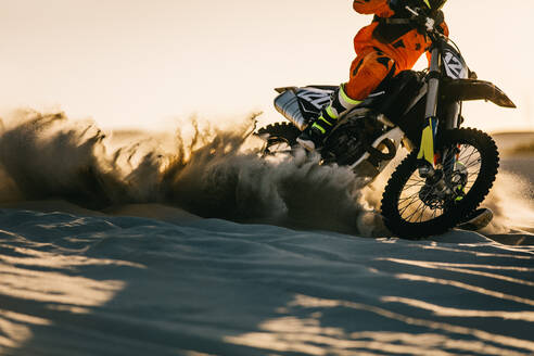 Motocross-Fahrer, der auf einer Sanddüne fährt, während hinter ihm Schmutz aufgewirbelt wird. Professioneller Dirt-Biker beim Training in der Wüste. - JLPSF15883