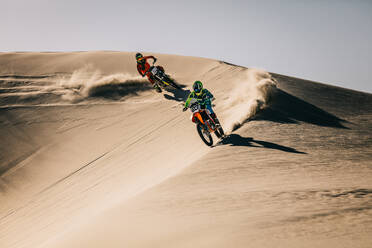 Motocross racers racing over off-road terrain. Dirt bikers riding motorcycles on sand dunes in a competition. - JLPSF15892