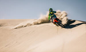 Motocross-Fahrer beim Beschleunigen in Sanddünen mit wegfliegenden Trümmern. Enduro-Fahrer in Aktion beim Beschleunigen des Motorrads nach der Kurve auf Sanddüne. - JLPSF15894