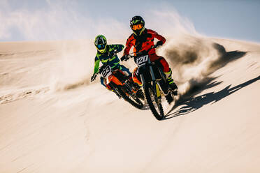 Zwei Dirt-Biker fahren auf Sanddünen und liefern sich ein intensives Motocross-Rennen. - JLPSF15898