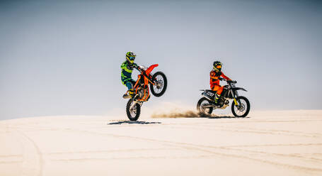 Two motocross riders riding bikes in desert. Professional dirt bikers diving motorcycle on sand dunes. - JLPSF15903