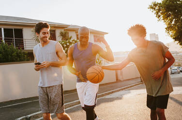 Drei Basketballer, die die Straße entlang gehen und mit dem Ball spielen. Männer, die nach einem Basketballspiel zurückgehen. - JLPSF15910