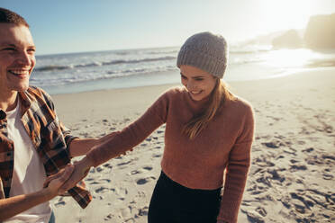 Happy young couple on the beach at evening. Man holding hand of young smiling at the sea shore. - JLPSF15924