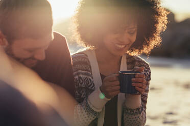 Schöne junge Frau, die mit einem männlichen Freund Kaffee trinkt. Lächelnde Freunde, die sich während des Sonnenuntergangs am Meer entspannen. - JLPSF15939